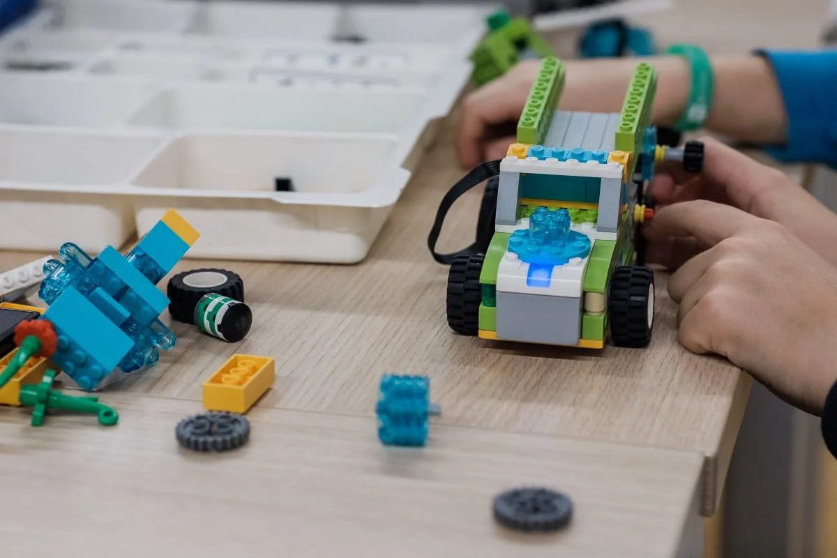 Zbudowany z klocków LEGO pojazd z silniczkiem i kołami zębatymi na stole podczas warsztatów z robotyki